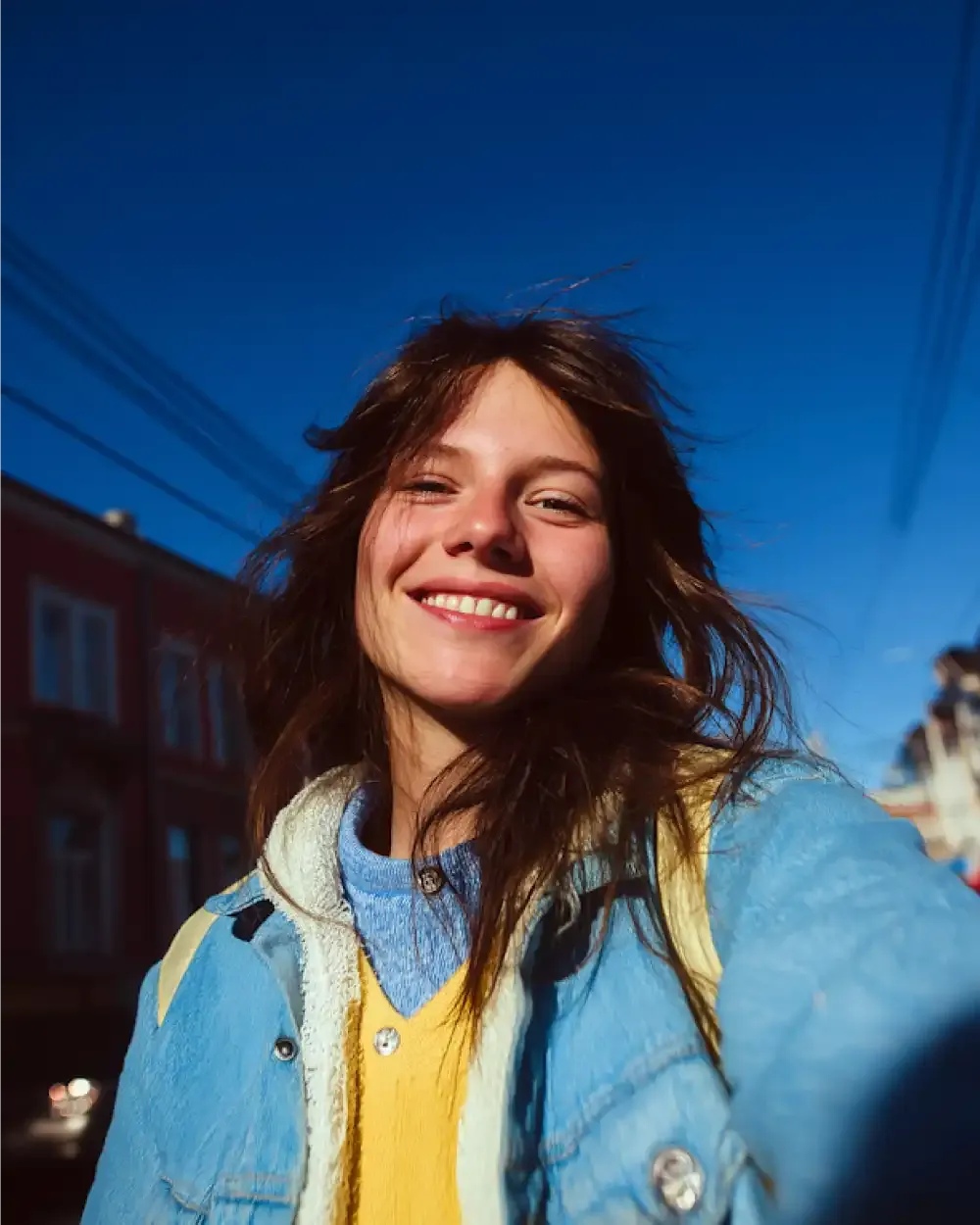 Joven sonriendo mientras se hace un selfie en la calle, disfrutando de la ciudad con la tranquilidad que da ēllu