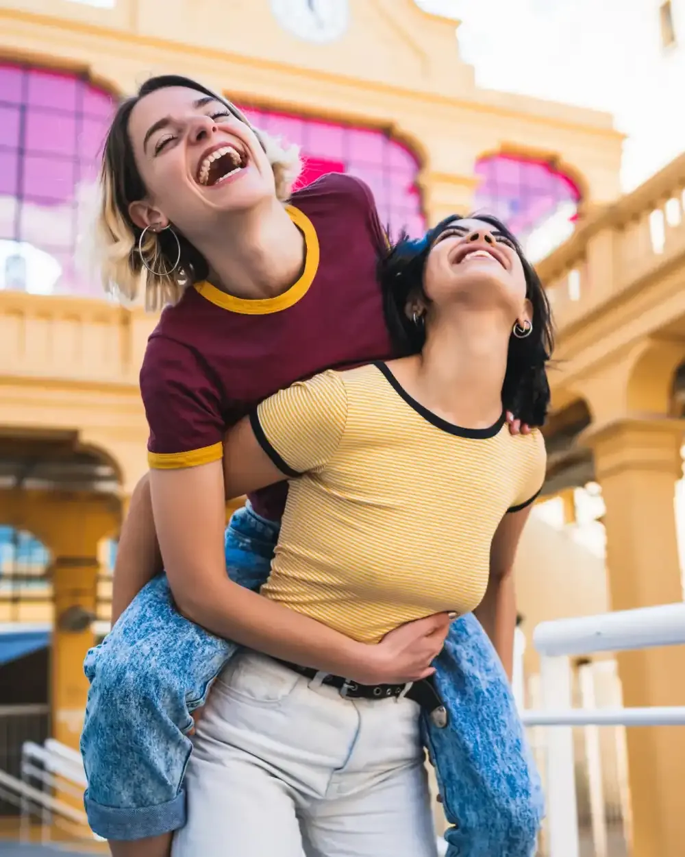 Dos amigas adolescentes riendo y disfrutando de su independencia en la ciudad, conectadas con sus familias a través de ēllu