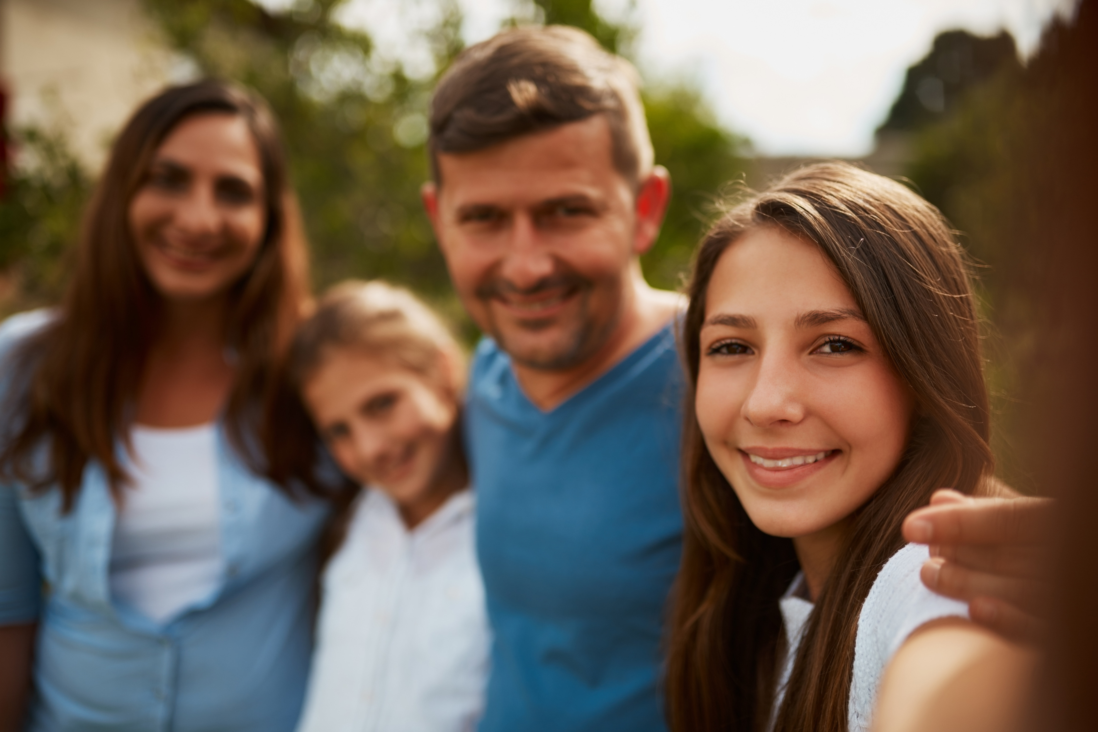Familia de cuatro personas tomándose una selfie sonriendo en un parque al aire libre, transmitiendo calidez, cercanía y vínculo familiar en un ambiente natural y luminoso.